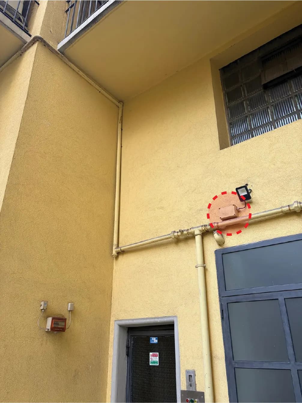 Facciata al piano terra con un cerchio rosso tratteggiato che indica il punto di ingresso proposto del cavo accanto alle tubazioni esistenti