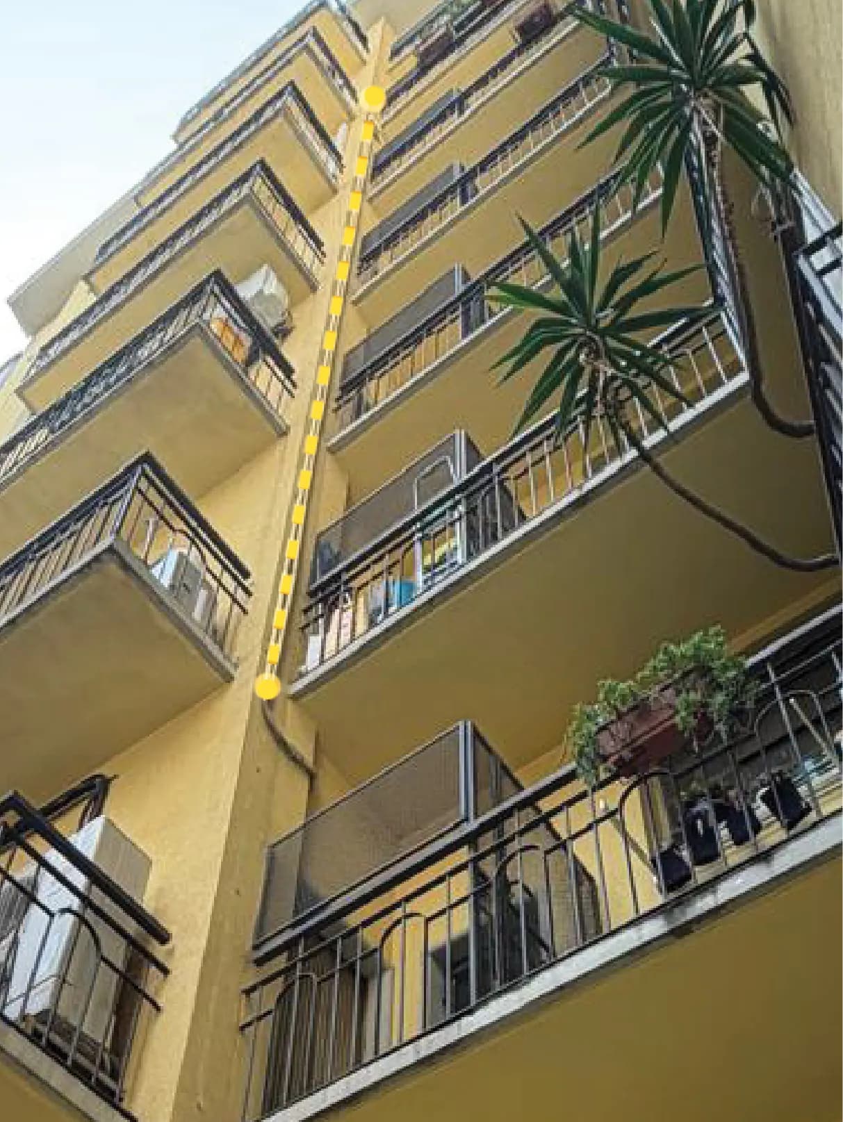 Fotografia dal basso della facciata gialla di un edificio residenziale con una linea gialla tratteggiata che indica il percorso proposto del cavo lungo i balconi